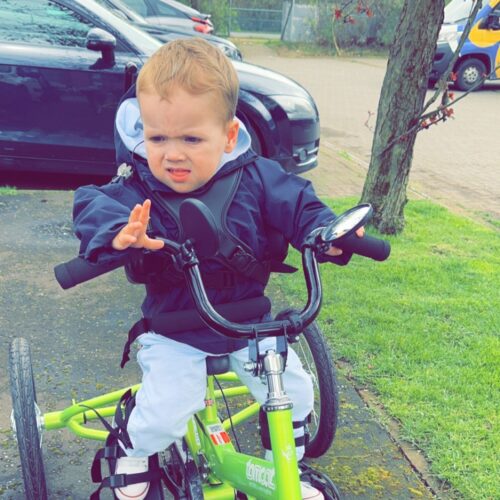 Four year old rides a green adapted trike